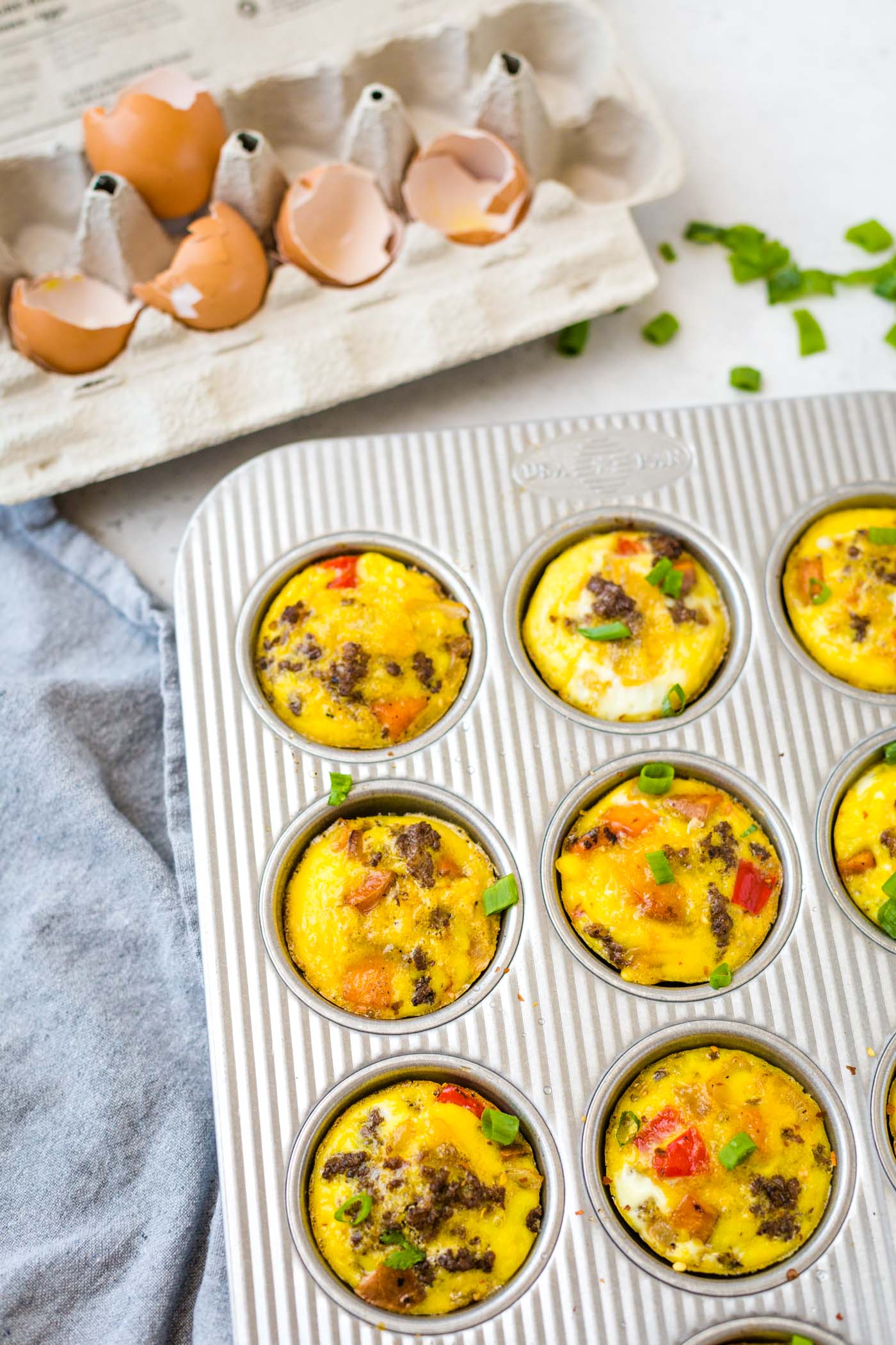 Whole30 Egg Muffins in muffin tin on white background with cracked eggs in egg carton