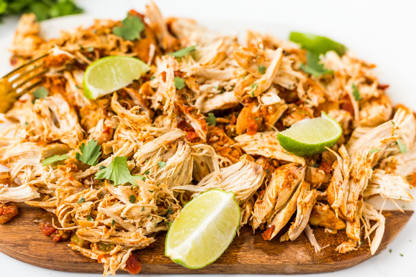 Shredded mexican chicken garnished with cilantro and sliced limes on cutting board