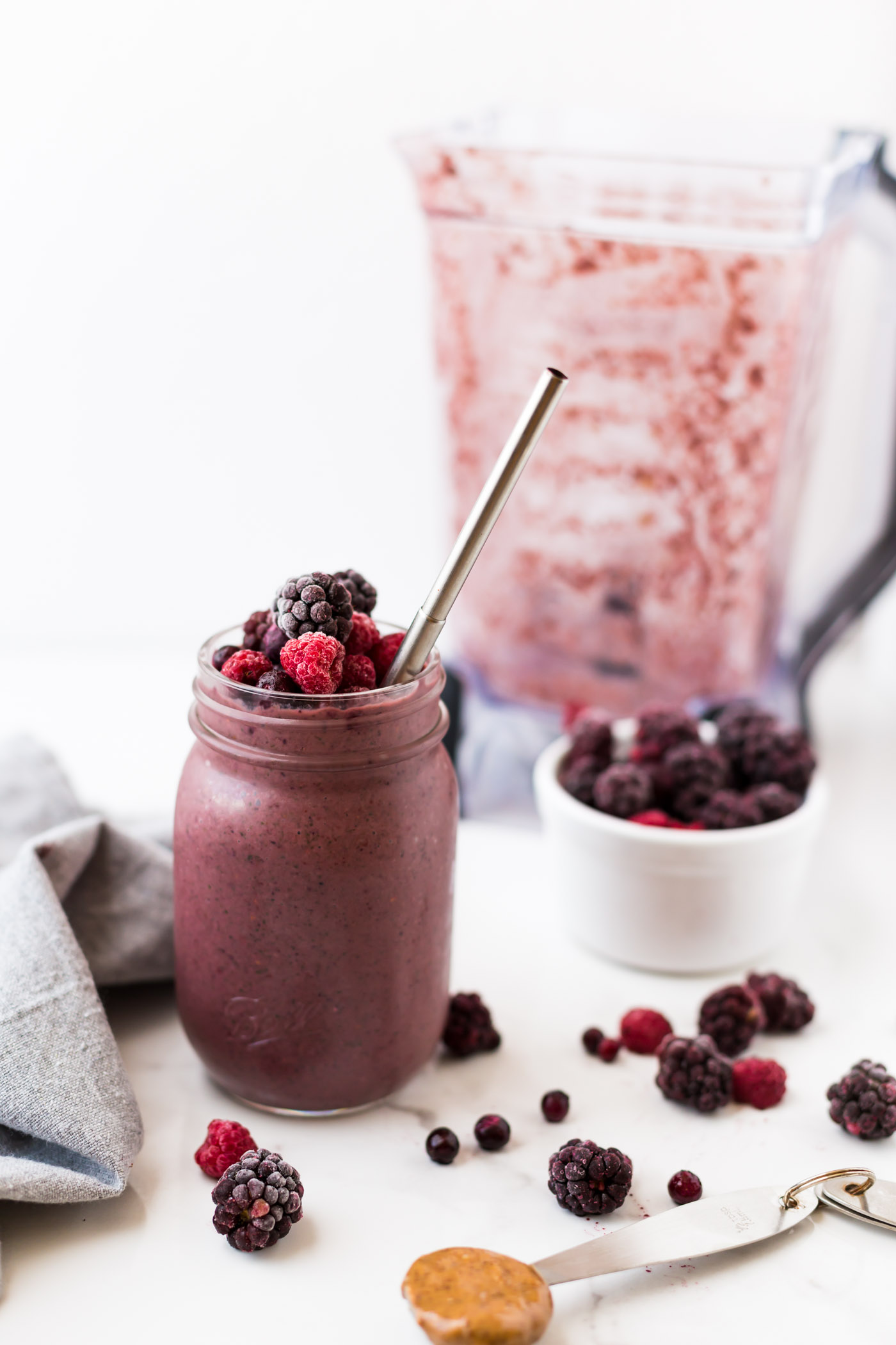 smoothie in mason jar topped with raspberries, blackberries, and blueberries on white background. 