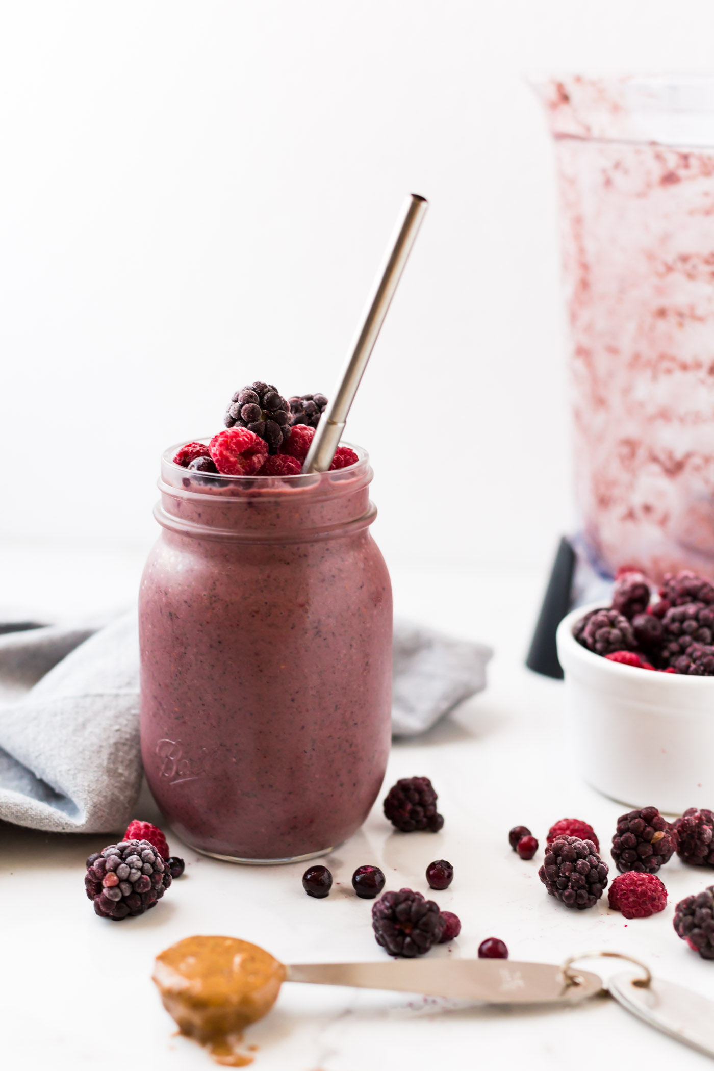 healthy mixed berry smoothie with scattered blackberries, blueberries and rasberries on white background