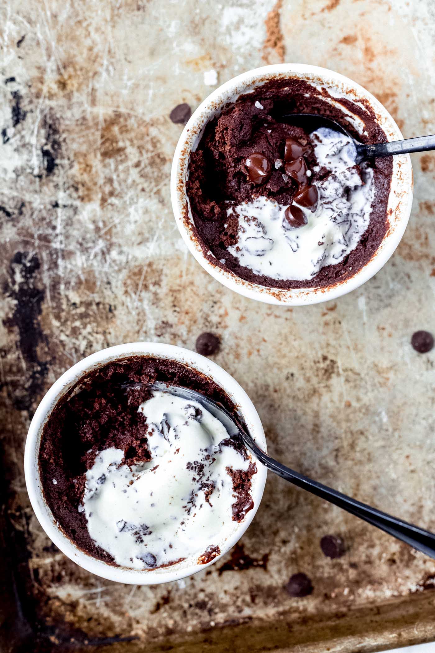 Gooey Brownie in a mug topped with vanilla ice cream and chocolate chips on baking sheet. 