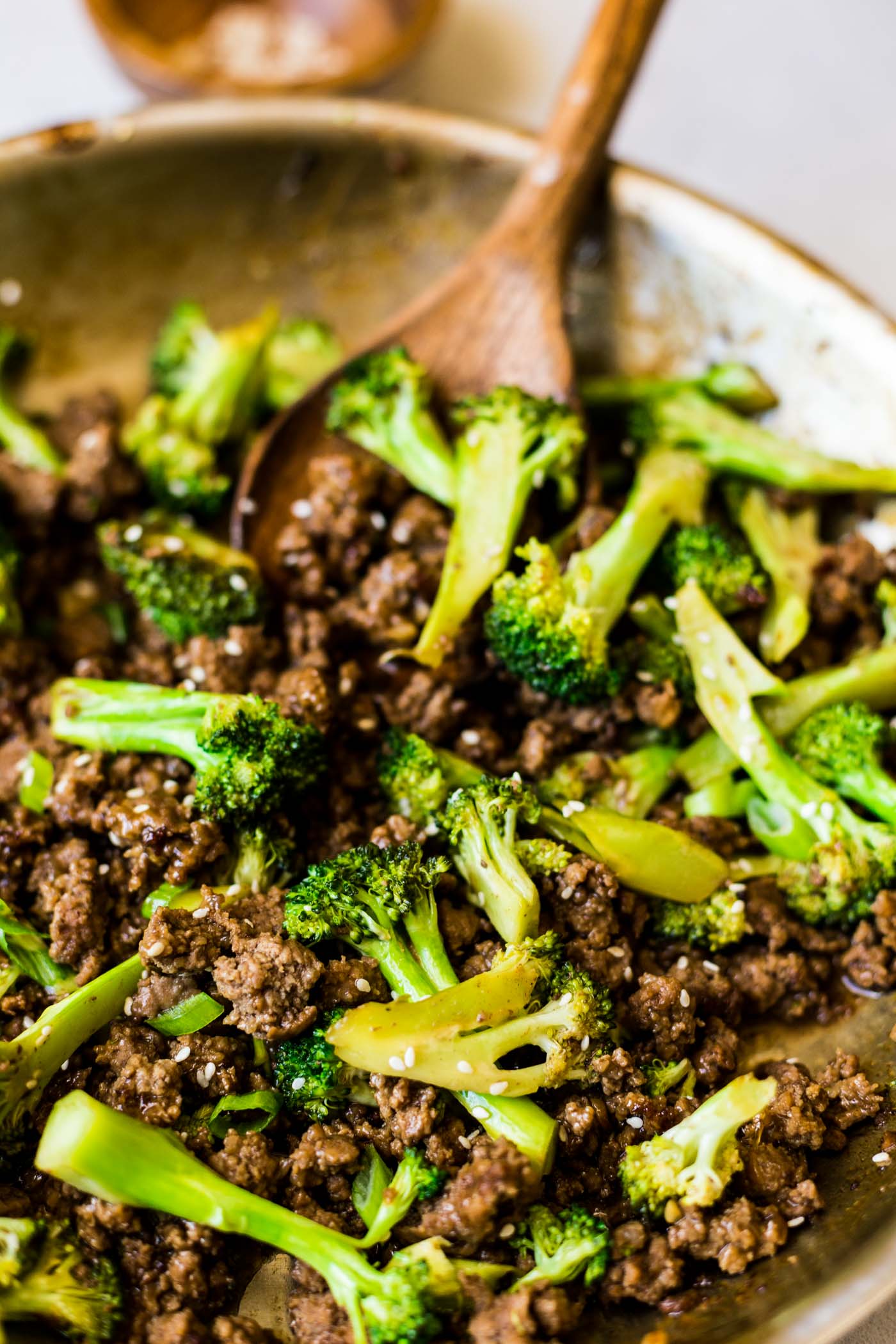 Wooden spoon scooping ground beef and broccoli in skillet