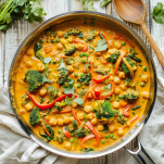 Overhead view of vegan coconut curry in a skillet with chickpeas, broccoli, and red bell peppers in a golden coconut milk sauce.