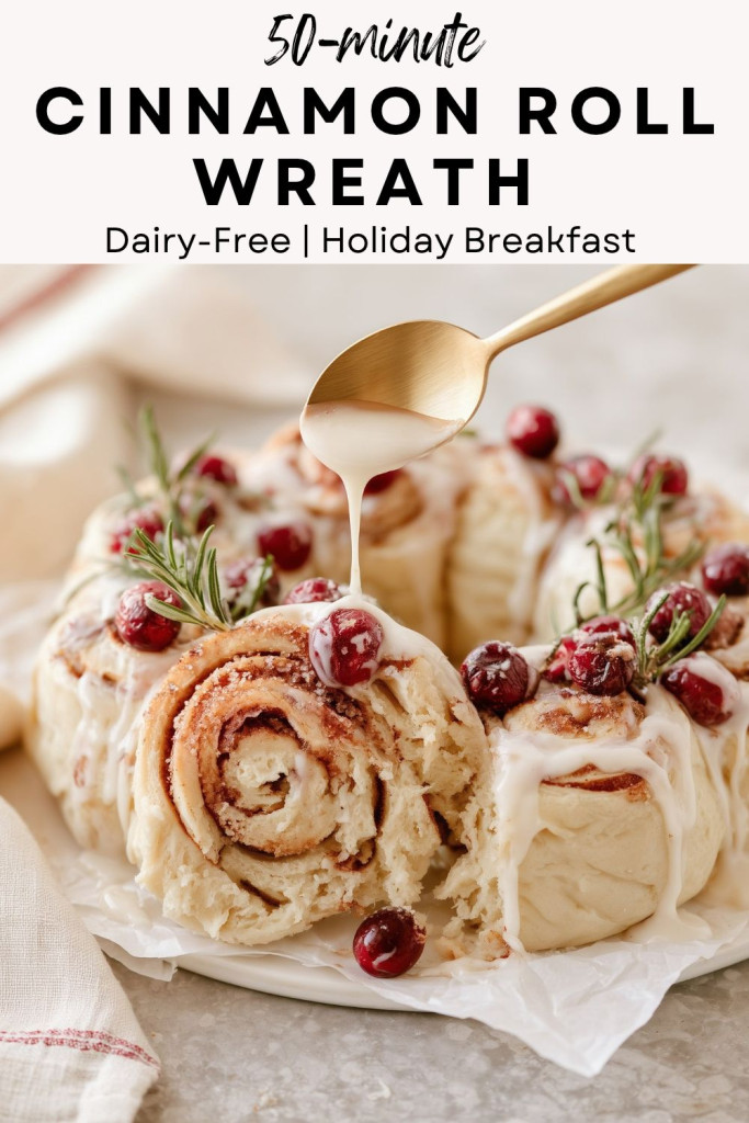 pinterest-ready image of glazed cinnamon roll wreath topped with cranberries and rosemary on parchment paper