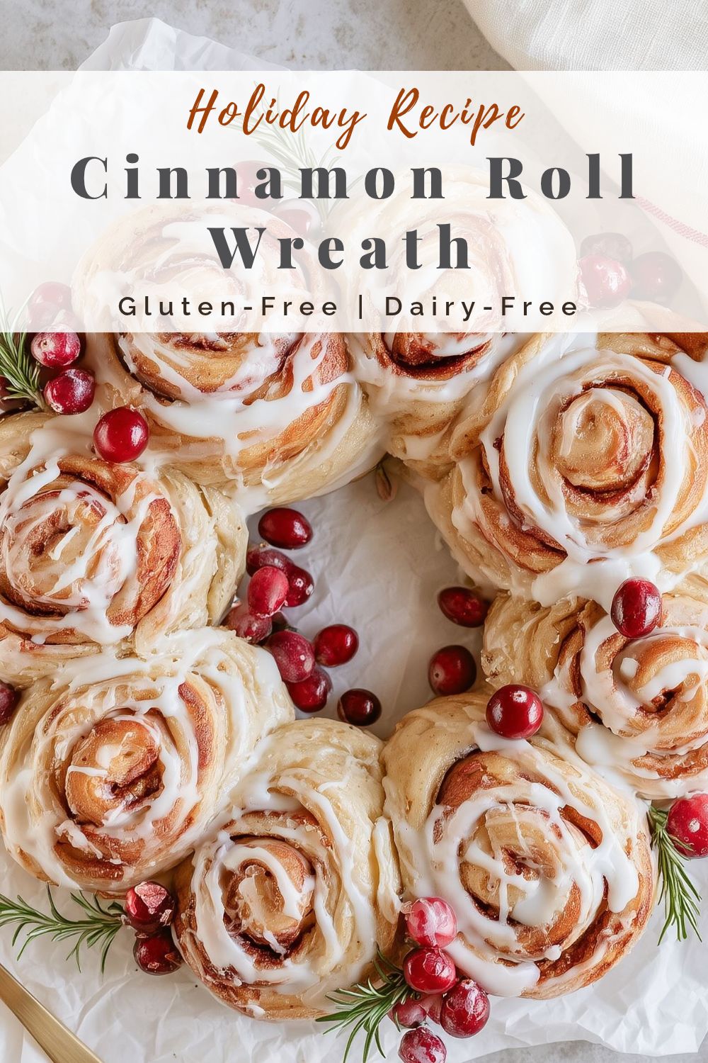 pinterest-ready image of glazed cinnamon roll wreath topped with cranberries and rosemary on parchment paper